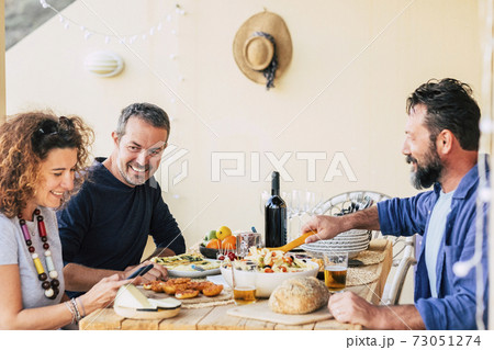 Group of adult caucasian friends enjoy lunch together at home outdoor - people enjoying food and drinks in leisure activity - friendship and cheerful people around a table with food 73051274