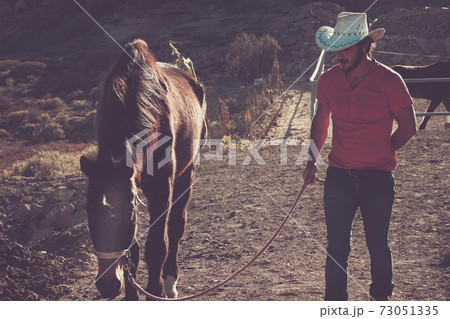 Man walk with a horse in country side farm and horses house - cowboy outdoor lifestyle with animals and freedom - alternative young people life 73051335