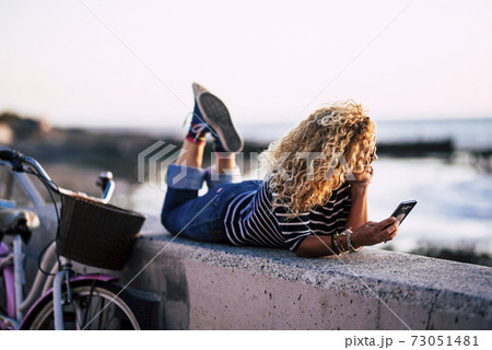 Beautiful blonde woman lay down outdoor enjoying relax and ocean view - active pretty people use mobile phone connection and look sea water in spring season Beautiful blonde woman lay down outdoor enjoying relax and ocean view - active pretty people use mobile phone connection and look sea water in spring season 73051481