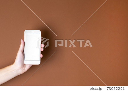 Touch screen mobile phone in hand on brown orange background. Minimal, stylish, trend concept. Copy space. Trend color 2021. 73052291