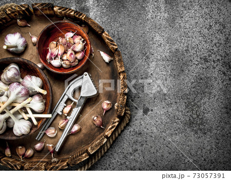 Fresh garlic in bowls with a press tool on a wooden tray. Fresh garlic in bowls with a press tool on a wooden tray. 73057391