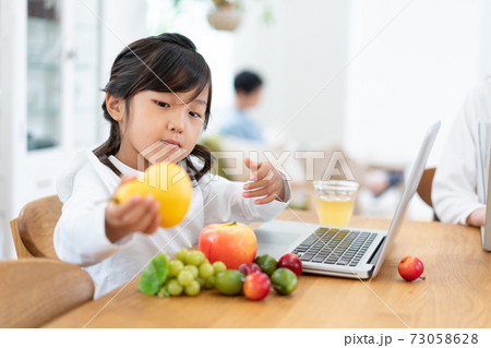 ダイニングでパソコンを見ながら果物のおもちゃで遊ぶ女の子の写真素材