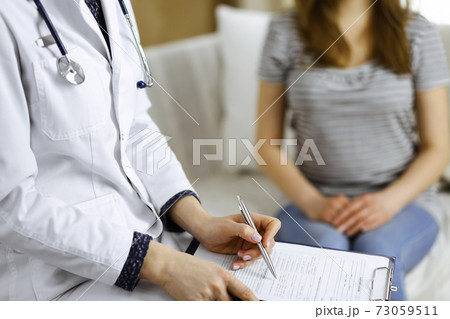 Unknown woman doctor and patient discussing current health examination while sitting in cozy living room. Stay at home concept during Coronavirus pandemic and self isolation quarantine 73059511