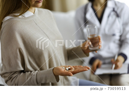 Close-up woman-patient holding pills near her doctor, time to take medications, cure for headache or remedy pain killer drugs. Stay at home concept during Coronavirus pandemic and self isolation 73059513