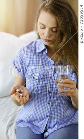 Young woman holding pills time to take medications, cure for headache, high blood pressure or cholesterol level remedy pain killer drugs 73059554