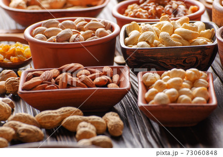 Assorted nuts and seeds in clay bowls on wooden kitchen table 73060848