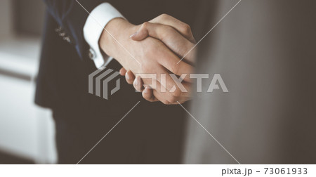 Unknown businessman shaking hands with his colleague or partner while standing straight in modern office, close-up. Business people group at meeting 73061933