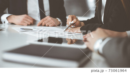 Unknown businessmen and woman sitting, working and discussing questions at meeting in modern office, close-up Unknown businessmen and woman sitting, working and discussing questions at meeting in modern office, close-up 73061964