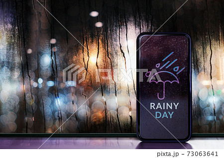 Rainy Day at Night in City Concept. Weather Forecast via Mobile Phone. Raindrops on Glass Window. Blurred Urban Lights as Outside View 73063641