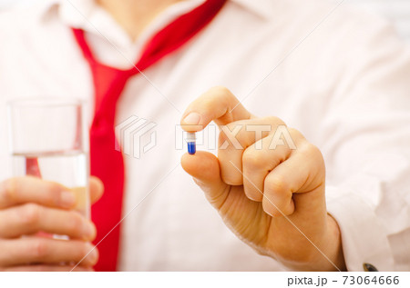 Caucasian male model holds blue pill and glass of water in his hands closeup 73064666
