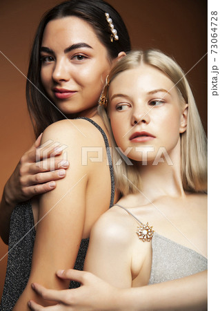 two pretty diverse girls happy posing together: blond and brunette on brown background, lifestyle people concept 73064728