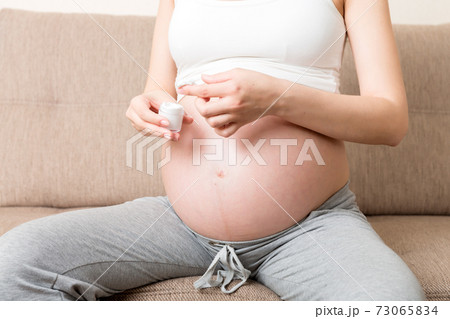 a pregnant girl sits at home on the bed and smears smile an anti-stretch mark cream on her stomach. Pregnancy, motherhood, preparation and expectation concept a pregnant girl sits at home on the bed and smears smile an anti-stretch mark cream on her stomach. Pregnancy, motherhood, preparation and expectation concept 73065834