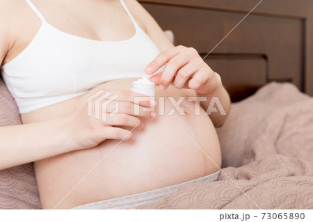 pregnant woman applying stretch mark cream to belly. pregnancy, people and maternity concept. pregnant apply anti-stretch mark cream on her belly 73065890