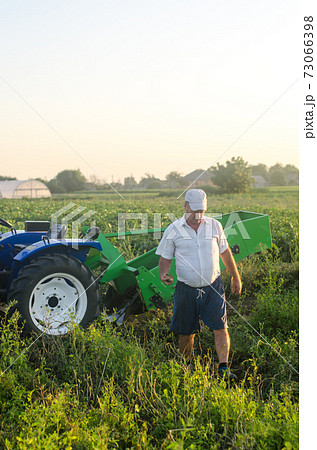 A farmer across the field from his tractor after harvesting. Extract root vegetables to surface. Work on small farms. Support and subsidies. End of the working day. Farming. Harvest potatoes in autumn 73066398