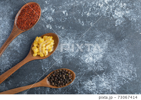Wooden spoons of corn kernels, ground and grain peppers on marble surface 73067414