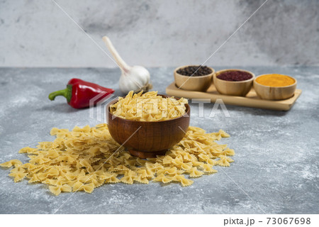 A wooden bowl full of raw macaroni and spices 73067698