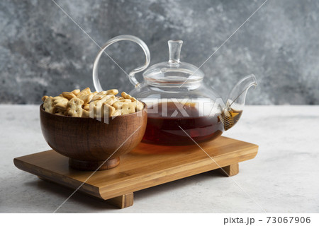 A glass teapot of tea with wooden bowl full of crackers 73067906