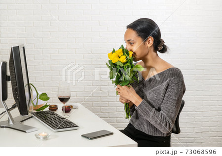 Young pretty mixed-raced woman holds a bunch of yellow roses in front of her face and speaking online 73068596