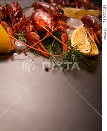 Boiled red crawfish, ready to eat with lemon slices and ice cubes on a black surface. 73070285