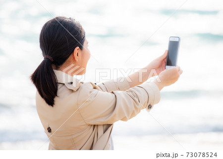 スマホで海の写真を撮る女性の写真素材