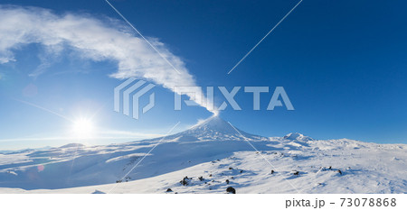 Winter volcanic landscape, panoramic view of eruption active volcano plume gas, ash from crater in sunny day with blue sky Winter volcanic landscape, panoramic view of eruption active volcano plume gas, ash from crater in sunny day with blue sky 73078868