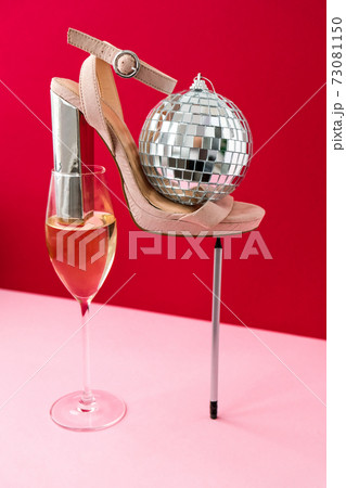 Trendy creative photo of Champagne glass with white wine and high heels in a modern balancing composition. Holiday party concept. Minimalistic concept in isometric style. Disco ball 73081150