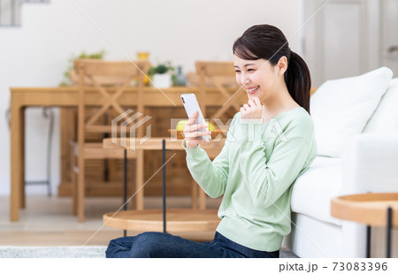 リビングでスマホを見る若い女性 73083396