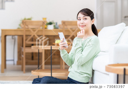 リビングでスマホを見る若い女性 73083397