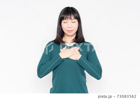白背景の前に立って胸に手を当てる女性 73083562