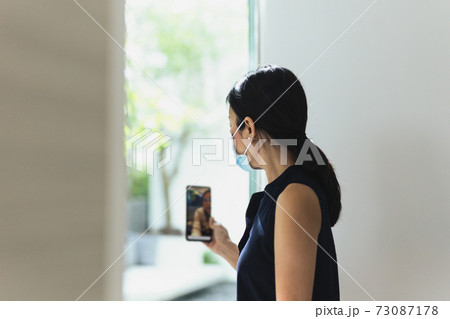 Businesswoman with protective mask work on video conference using mobile phone. 73087178