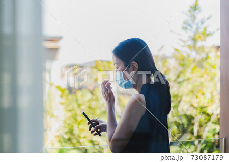 Woman in medical mask self quarantine at home make video call on cell phone with family. 73087179