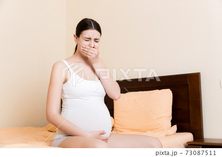 Pregnant suffering with nausea. Pregnancy symptoms, expectation toxicosis. Young vomiting woman sitting on bed. parenthood concept Pregnant suffering with nausea. Pregnancy symptoms, expectation toxicosis. Young vomiting woman sitting on bed. parenthood concept 73087511