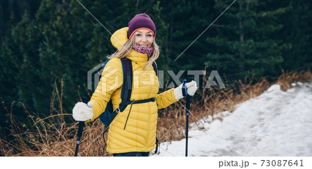 Smiling blond tourist in yellow jacket on winter trail in mountains. 73087641