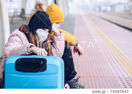 Sad children are sitting on the platform of the train station wanting to go on winter holidays. 73087642
