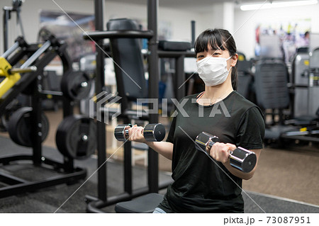 マスクしてフィットネスジムで筋トレをする女性 73087951