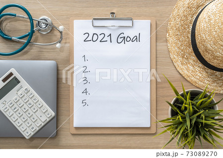 2021 goals on clipboard medical note pad for new year reminder list of yearly planner, health plan for work-life balance on desk background with computer, calculator, travel hat 73089270