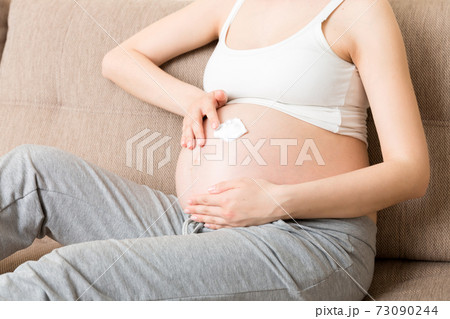 a pregnant girl sits at home on the bed and smears an anti-stretch mark cream on her stomach. Pregnancy, motherhood, preparation and expectation concept 73090244