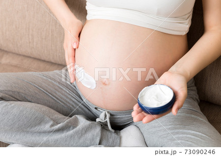 a pregnant girl sits at home on the bed and smears smile an anti-stretch mark cream on her stomach. Pregnancy, motherhood, preparation and expectation concept a pregnant girl sits at home on the bed and smears smile an anti-stretch mark cream on her stomach. Pregnancy, motherhood, preparation and expectation concept 73090246