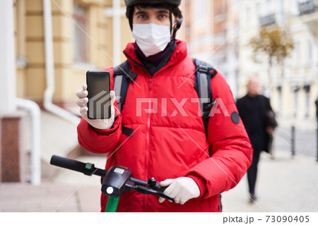 Delivery food courier guy showing smartphone screen at the camera 73090405