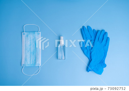 A set of personal hygiene items from a medical mask, gloves and a disinfector on a blue background. COVID-19 pandemic. Remedies 73092752