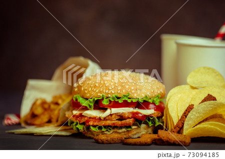 Burger on a rustic wooden board and unhealthy snacks and chips 73094185