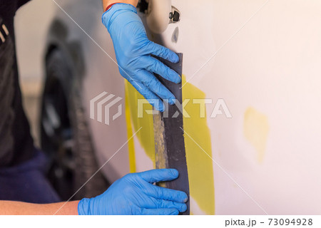 Repairing car body, Application putty close up. The mechanic repair the car. Work after the accident by working sanding primer before painting. 73094928