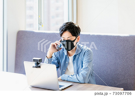 カフェでパソコンを見ながらスマホで会話するマスクの男性 カフェでパソコンを見ながらスマホで会話するマスクの男性 73097706