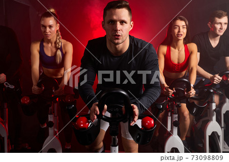 muscular young caucasian man exercising cardio training on bicycle in fitness gym with friends 73098809