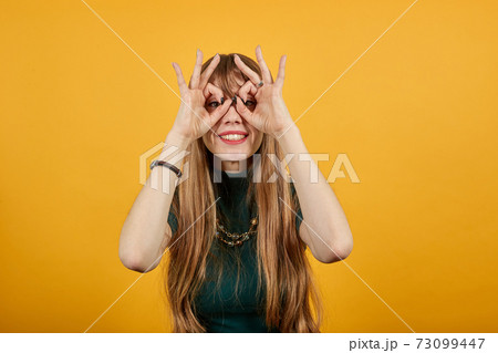 Making glasses fingers, looking at camera, smiling, funny, hold hands near eyes 73099447