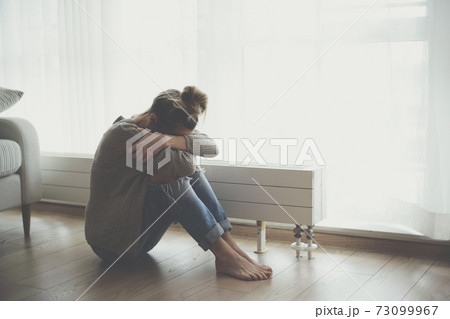 A lonely young woman feels depressed and stressed as she sits on the floor with her head in her hands. 73099967