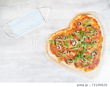 Heart shaped vegetarian pizza with medical mask on grey table Heart shaped vegetarian pizza with medical mask on grey table 73100620