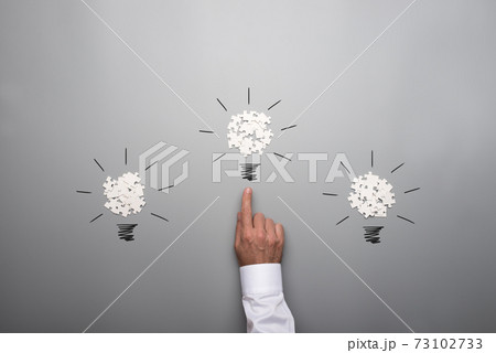 Three light bulbs formed by scattered white puzzle pieces with hand of a businessman 73102733