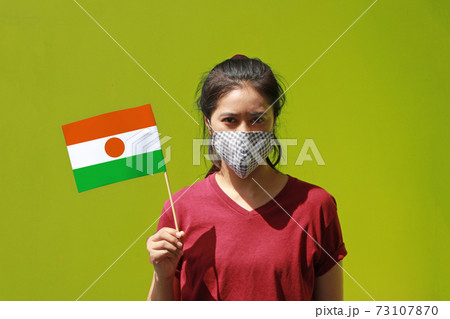 Masked woman in brown shirt and Niger flag in hand on green background. Masked woman in brown shirt and Niger flag in hand on green background. 73107870