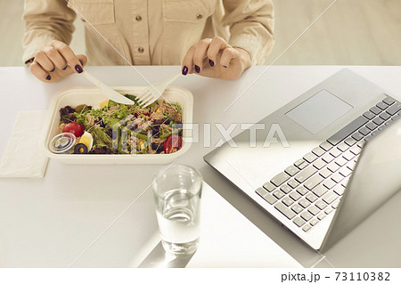 Busy student having healthy takeaway lunch from meal container during working day 73110382